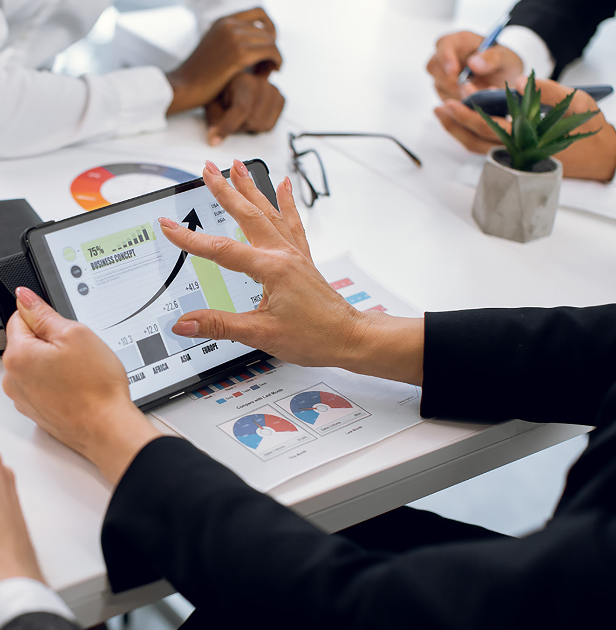 Cropped close up image of unrecognizable multiracial businesspeople having meeting at office. Focus on female hands touching digital tablet pc with business diagram infographics.