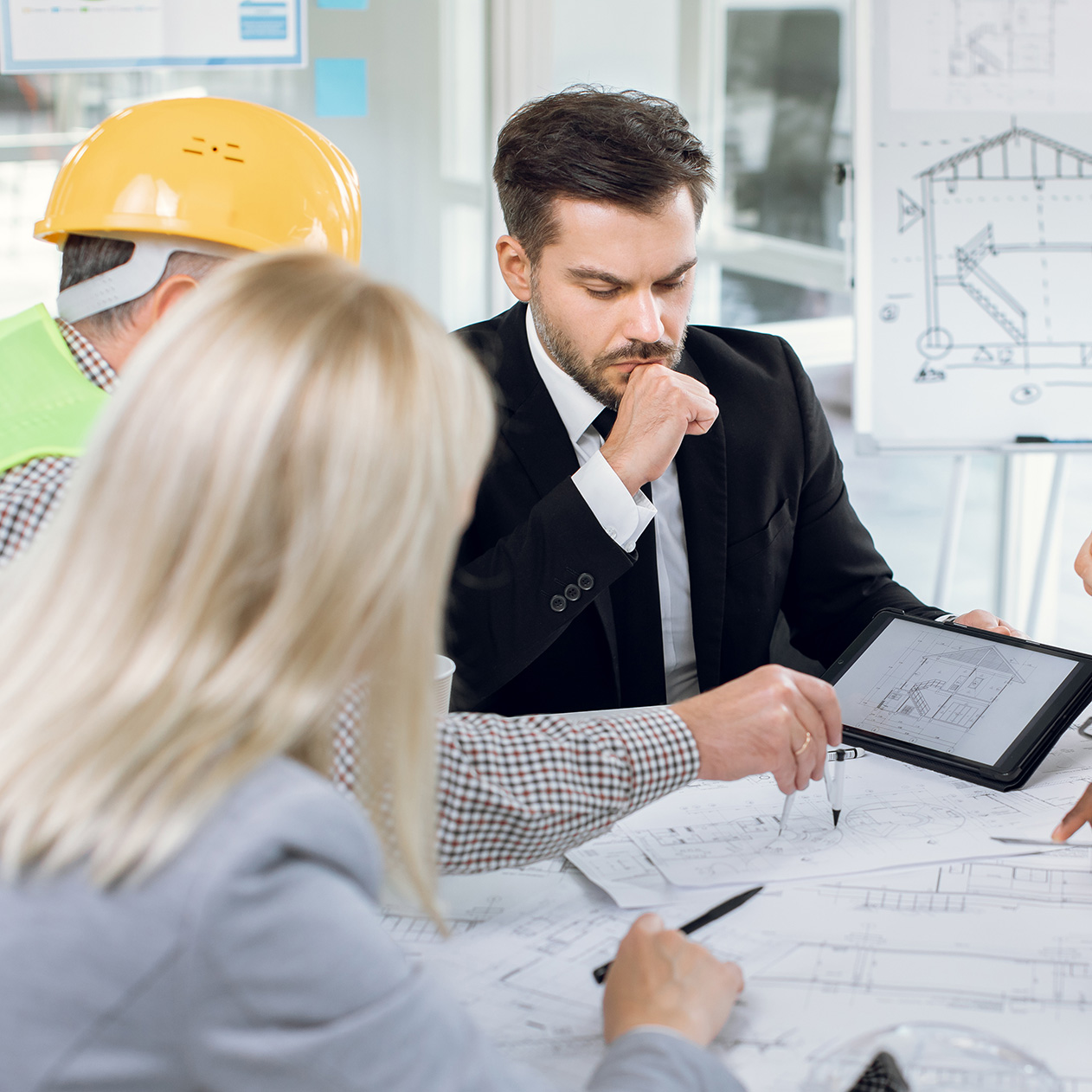 Multiracial office workers in suits and helmets having conference about construction project. Men and women cooperating to create new modern high-rise building.